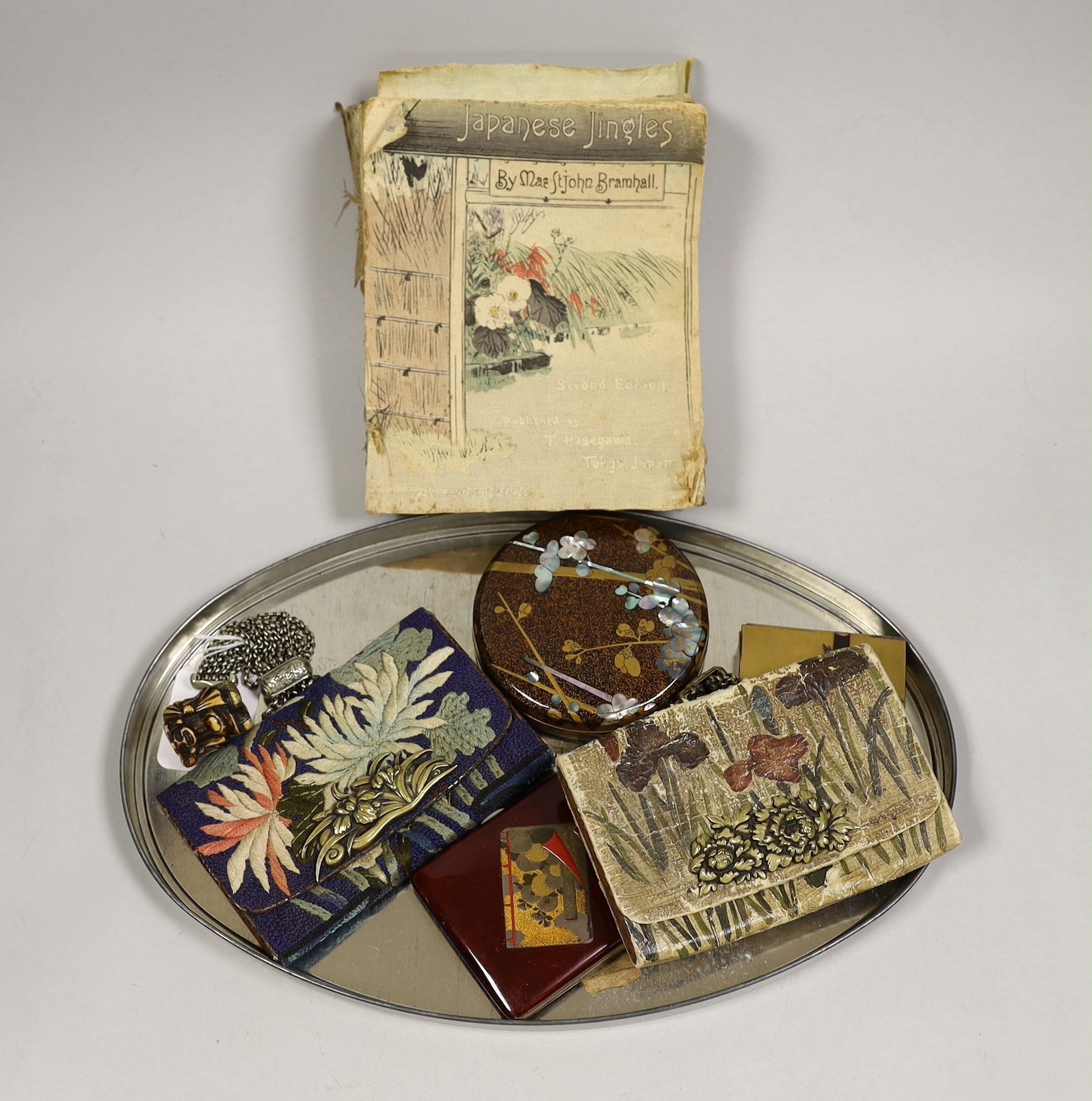 Two crepe paper Japanese illustrated books, a Japanese enamel compact two lacquer boxes and covers and two Japanese tobacco pouches, one with ivorine manju netsuke and the other a carved staghorn netsuke of Daikoku